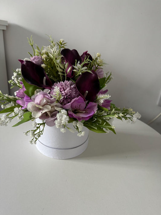 White hat box, filled with artificial greenery, lilac flowers and deep purple calla Lillies.