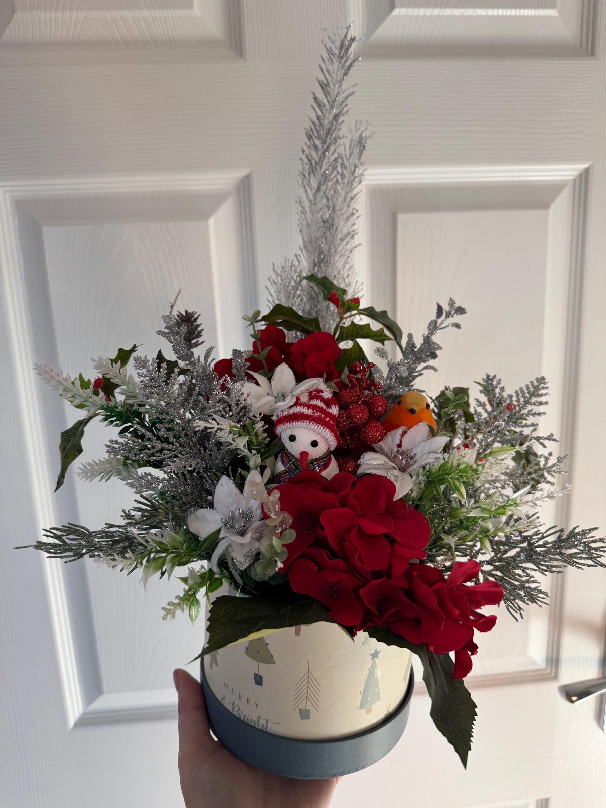 Small Christmas hat box filled with red artificial flowers and silver foliage. It comes with a snowman and a robin